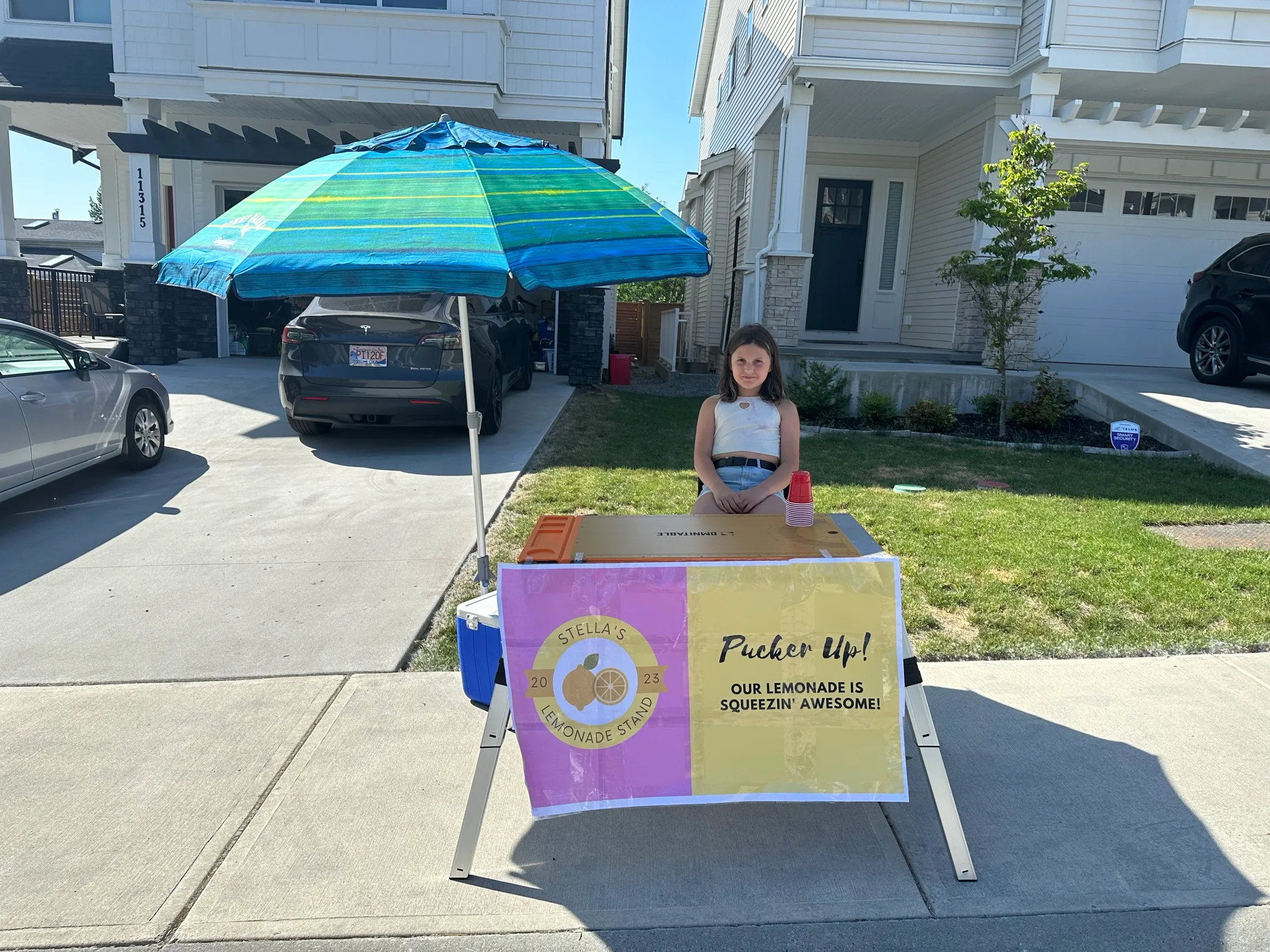 Stella smiling at her lemonade stand on opening day, with the Pucker Up! banner.
